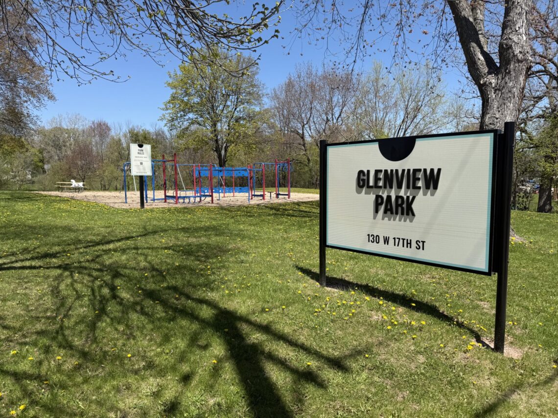 Picture of a sign for Glenview Park with blue and red playground equipment in the background.