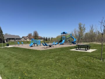 Picture of a park with blue, green and purple playground equipment and a picnic table.
