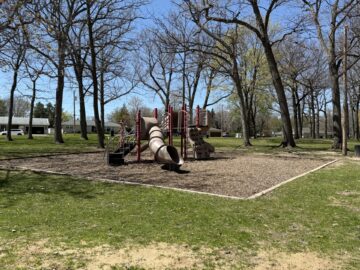 Picture of tan and red playground equipment with plenty of shade trees
