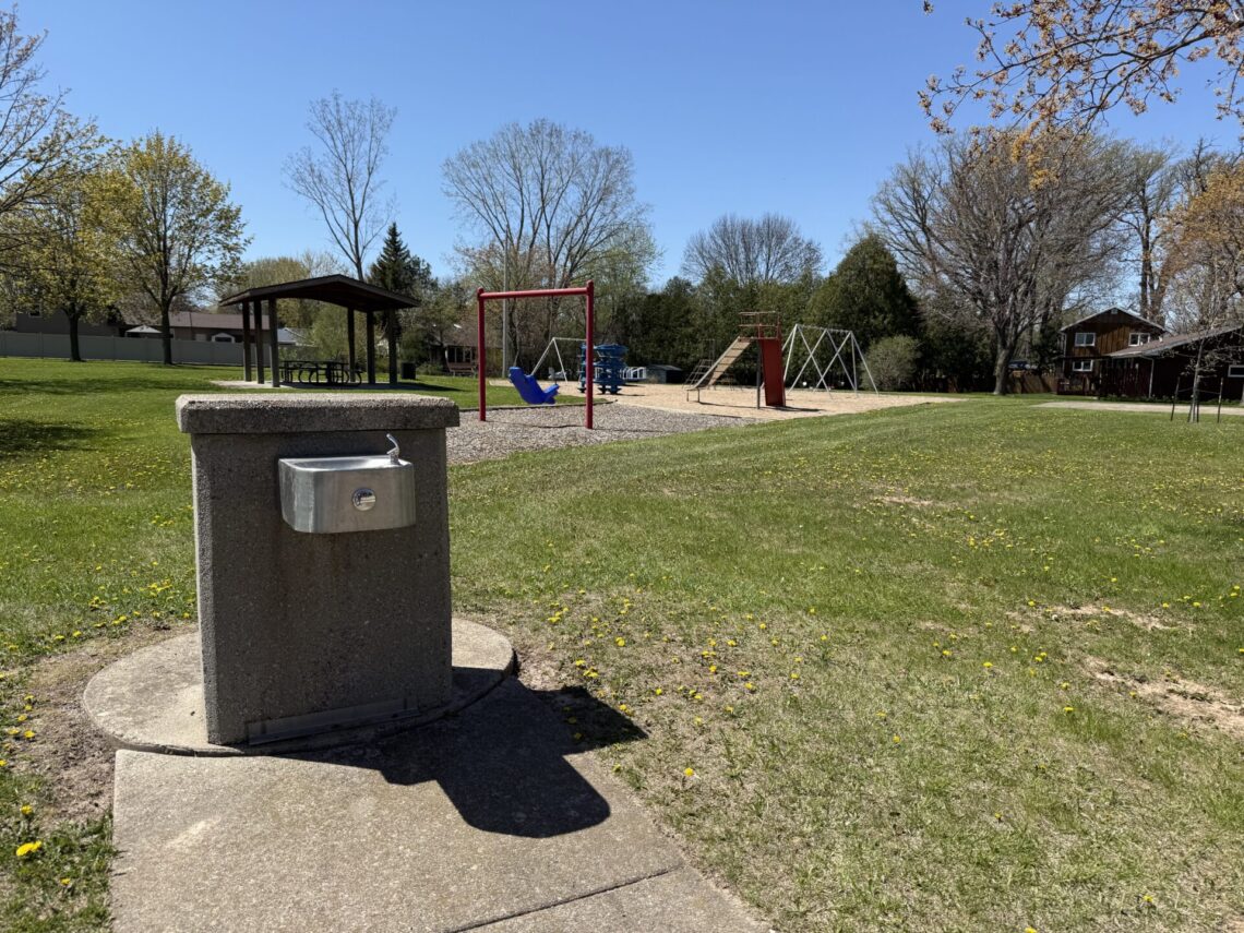 Picture of a drinking fountain with red and blue playground and swings in the background