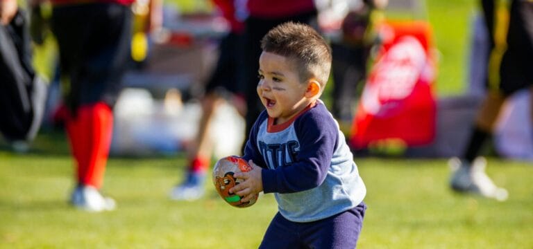Stock image of small child playing with a football by Photo by Sides Imagery