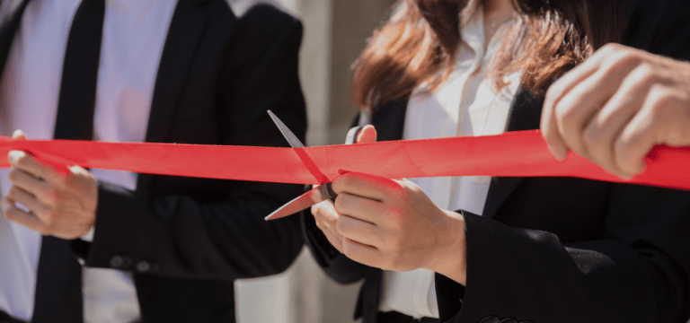 Stock image of people in suits cutting a red ribbon with a scissors
