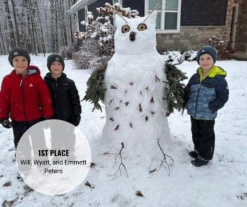 Three children stand next to a snowman in the shape of an owl with branches for wings