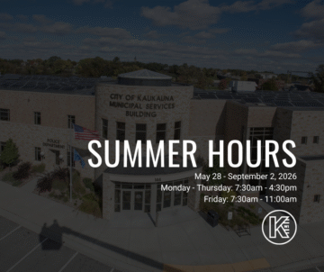 The image shows the City of Kaukauna Municipal Services Building with a brick exterior. Flags are positioned near the entrance. Overlay text displays summer hours: May 28 - September 2, 2026, Monday to Thursday 7:30am - 4:30pm, Friday 7:30am - 11:00am. A City of Kaukauna is in the bottom right corner.